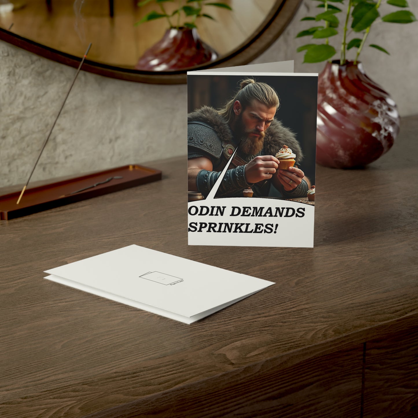 Greeting card with a Viking holding a cupcake on a wooden surface with decorative items.